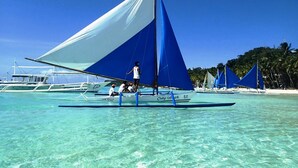 A clear tropical beach with a sailboat and other boats in shallow waters. - Aquarius Terraces Boutique Resort (Boracay Island)