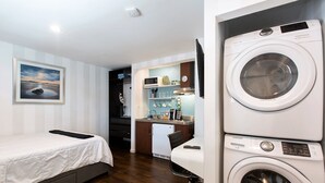 Une chambre d’hôtel équipée d’un lit, d’un bureau avec un ordinateur, d’une machine à laver et d’un petit coin cuisine.
