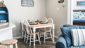 Ein Essbereich mit einem Holztisch und weißen Stühlen, einem blauen Sofa und einer Wand mit dem Schriftzug "Life is good at the beach".