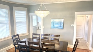 A dining room with a wooden table and chairs, a chandelier, and a painting on the wall.