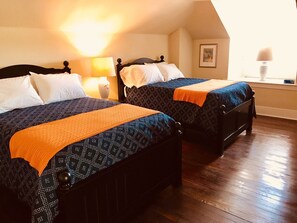 Two beds with patterned bedding and orange throw blankets, a nightstand with a lamp, and a framed picture on the wall.