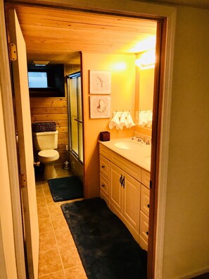 A narrow bathroom with a toilet, sink, and mirror. There are two framed pictures on the wall.