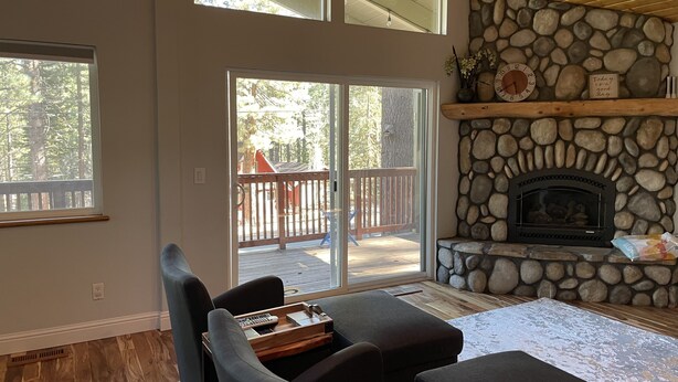 A spacious living area with a stone fireplace, large windows, and a view of the outdoor deck.