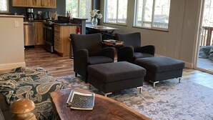 A spacious living area with a wooden ceiling, large windows, a kitchen, and a cozy seating arrangement.