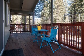 A wooden deck with a table and chairs, a yellow watering can, and a red railing.