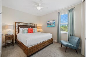 A bedroom with a wooden bed, a nightstand, a chair, a ceiling fan, a window with curtains, and a painting on the wall. - Access to 3 Private GOLF COURSES+Waterpark+POOL & SPA+Gameroom+THEATER+Disney (Four Corners)