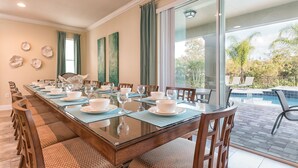 Comedor con una larga mesa dispuesta para una comida, ventanas amplias y vistas a una piscina.