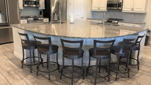 Una cocina moderna con encimeras de granito, electrodomésticos de acero inoxidable y una isla central con taburetes de bar.
