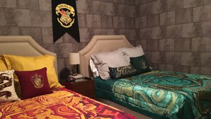 Una habitación con dos camas, cada una con ropa de cama y almohadas temáticas, una mesita de noche con lámpara, y un cartel en la pared.