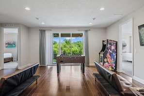 A room with a pool table, seating area, and arcade machine.