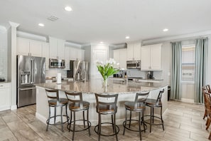 A modern kitchen with white cabinetry, stainless steel appliances, a granite island with bar stools, and a vase of flowers. - Access to 3 Private GOLF COURSES+Waterpark+POOL & SPA+Gameroom+THEATER+Disney (Four Corners)