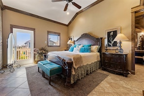 A bedroom with a large bed, a dresser, a bench, and a ceiling fan.