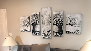 Uma sala de estar com um sofá cinza, uma mesa de centro e uma obra de arte na parede.