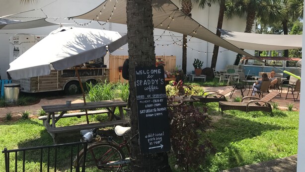 Um café com mesas ao ar livre, uma placa e uma bicicleta estacionada perto.