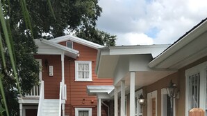 Uma casa de dois andares com varanda coberta, um caminho de concreto e um jardim com arbustos e uma mangueira.