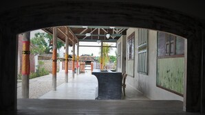Un espacio al aire libre techado, con piso de concreto, pilares de madera y una barra negra.