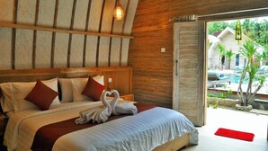 Una habitación de hotel con cabecera de madera, cama con sábanas blancas, almohadas rojas y un tapete rojo en el suelo.