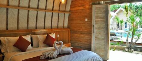 Une chambre d’hôtel avec une tête de lit en bois, un lit recouvert de draps blancs, des oreillers rouges et un tapis rouge sur le sol.