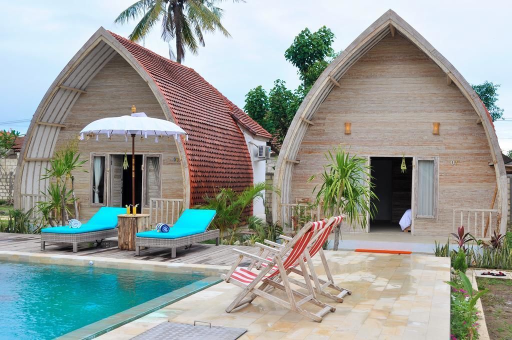 Two wooden cottages with pitched roofs, a swimming pool, and lounge chairs.