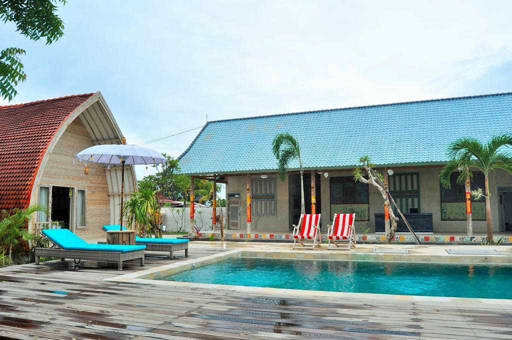 Une piscine avec des chaises longues et des parasols, un bâtiment doté d’un toit en tuiles et des palmiers.