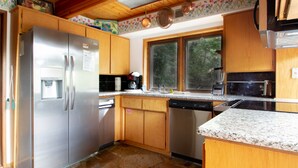 Una cocina con gabinetes de madera, un refrigerador de acero inoxidable, un lavavajillas y una ventana con vista a árboles.