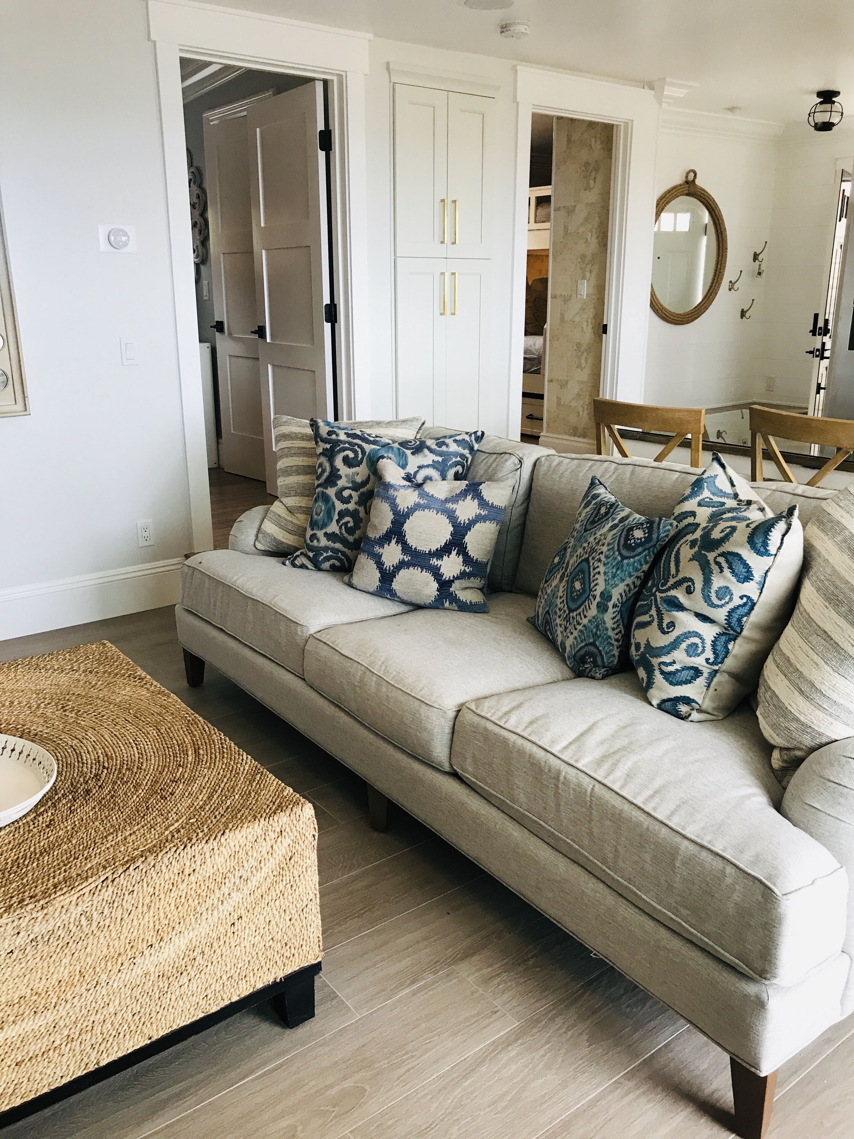 Una sala de estar con sofá color beige, cojines estampados, una mesa de centro tejida y piso de madera.