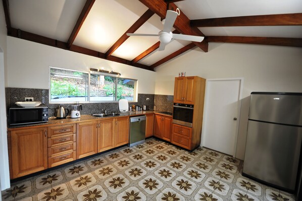 Una cocina con armarios de madera, microondas, refrigerador y ventilador de techo.