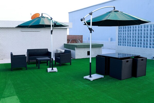 An outdoor patio with a green artificial turf, a black sofa set, a glass-top table, and two umbrellas. - Résidence Ethan (Abidjan)