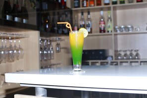 A bar setting with a tall glass of a green and yellow drink, a lemon slice garnish, and a straw. - Résidence Ethan (Abidjan)