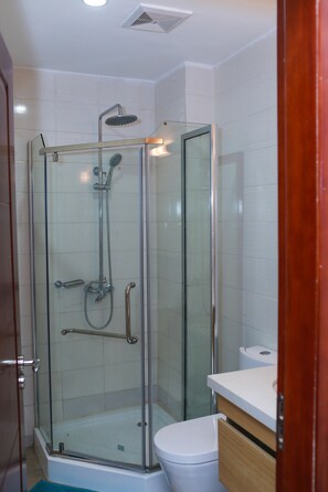 A glass-enclosed shower with a handheld showerhead, a handheld faucet, and a glass door. - Résidence Ethan (Abidjan)
