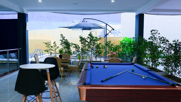 A pool table with pool balls, surrounded by chairs and tables, in a room with a glass partition and a view of the outside. - Résidence Ethan (Abidjan)