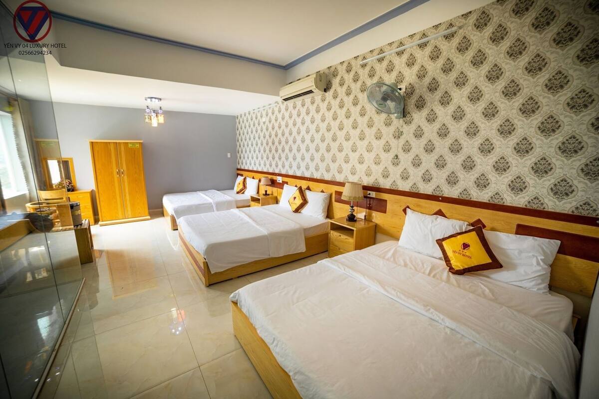 Habitación de hotel con tres camas, un armario de madera, un espejo y un papel tapiz estampado.