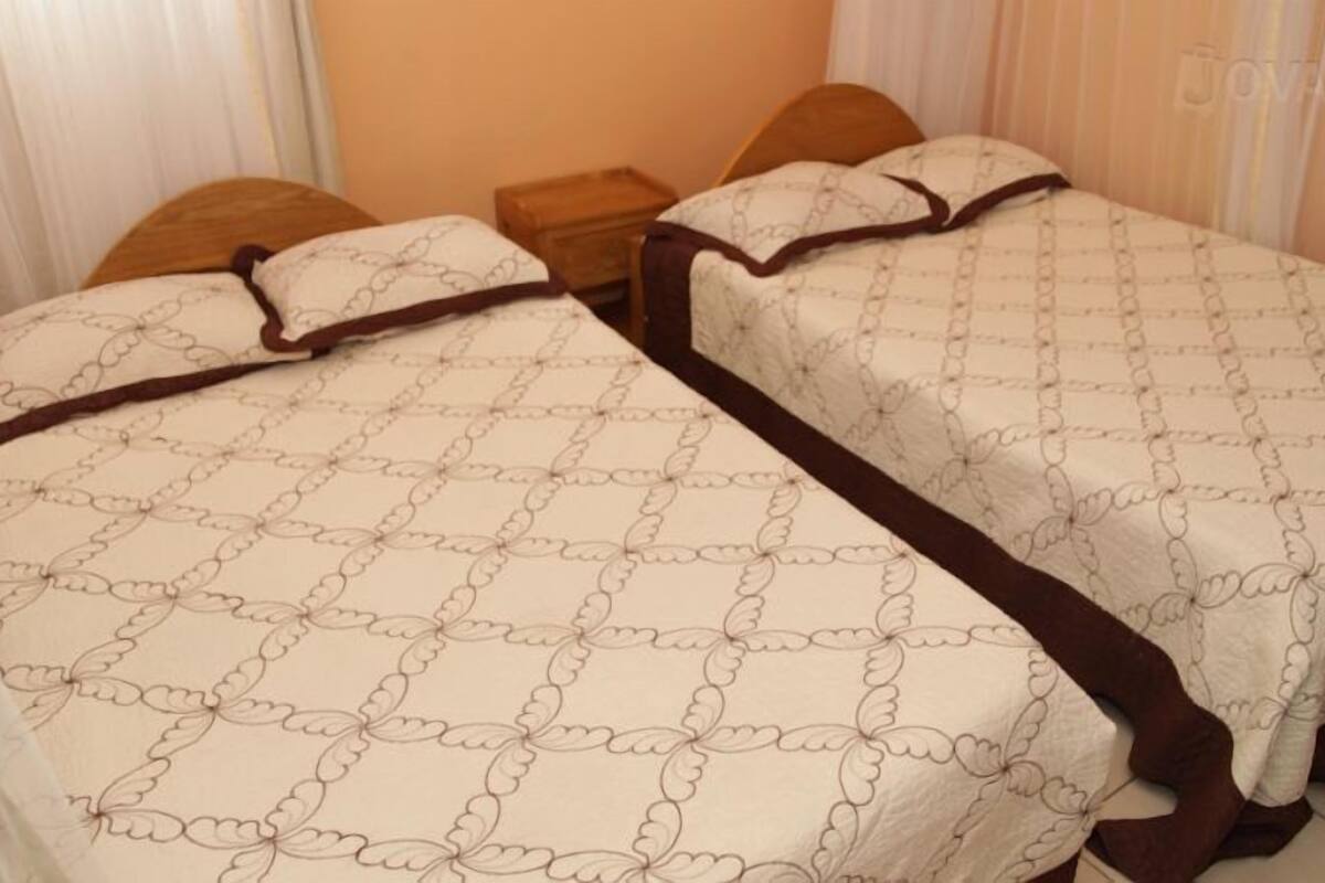 A double bed with a patterned bedspread and two pillows, a wooden nightstand, and a headboard.