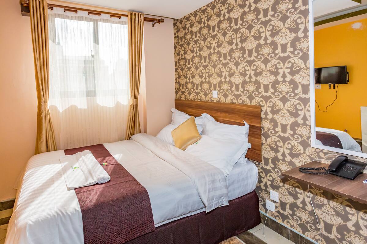 A neatly made bed with a headboard, a bedside table with a phone, and a patterned wall.