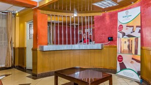 A reception area with a wooden reception desk, a digital screen, and a poster advertising Hotel Green. - Hotel Green Court Nairobi (Nairobi)