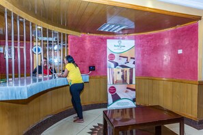 A reception area with a counter, a woman at the counter, and a poster advertising Hotel Green. - Hotel Green Court Nairobi (Nairobi)