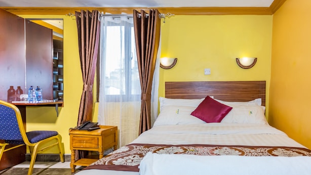 A hotel room with a bed, a desk with a chair, a telephone, and a shelf with bottles. - Hotel Green Court Nairobi (Nairobi)