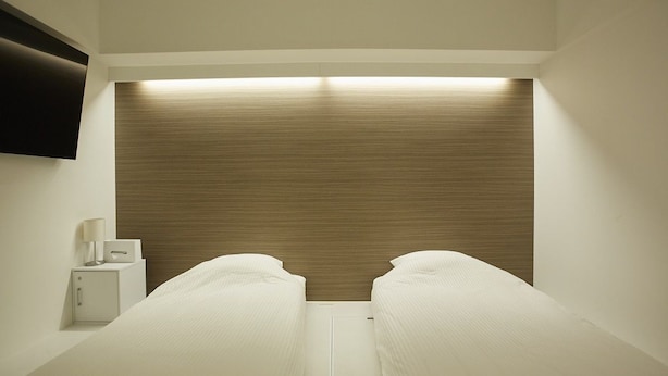 A hotel room with two single beds, a bedside table with a lamp, and a flat-screen TV mounted on the wall. - IN FRAME HOSTEL enoshima - Hostel (Fujisawa)