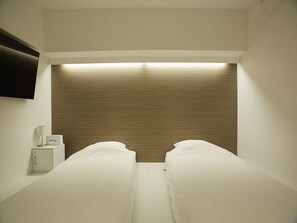 Een hotelkamer met twee eenpersoonsbedden, een nachtkastje met een lamp en een aan de muur bevestigde flatscreen-tv.