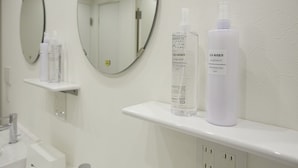 A bathroom with two round mirrors, a sink, and shelves holding toiletry bottles. - IN FRAME HOSTEL enoshima - Hostel (Fujisawa)