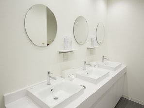 Un baño moderno con tres lavamanos, dos espejos redondos y una encimera blanca.