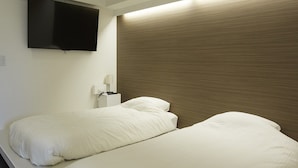 A hotel room with two beds, a flat-screen TV mounted on the wall, and a bedside table with a lamp. - IN FRAME HOSTEL enoshima - Hostel (Fujisawa)