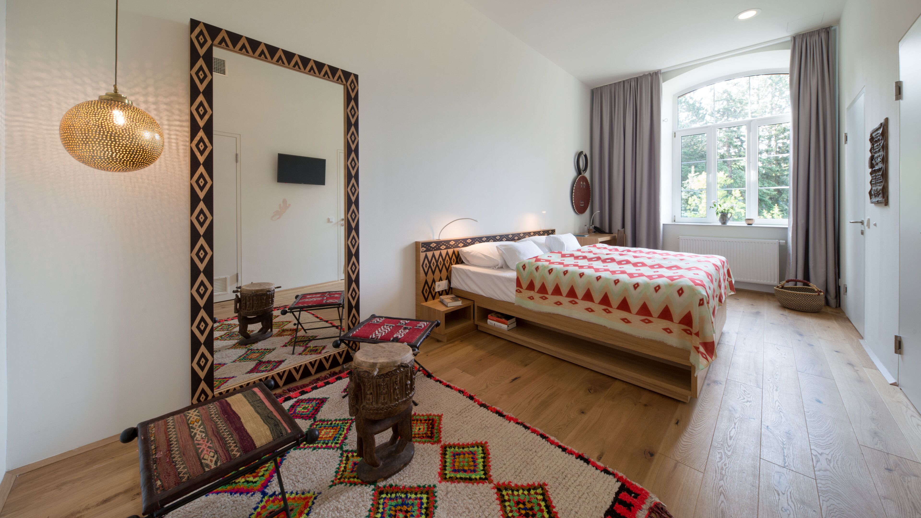 A bedroom with a bed, a large mirror, a television, a window with curtains, and a patterned rug.
