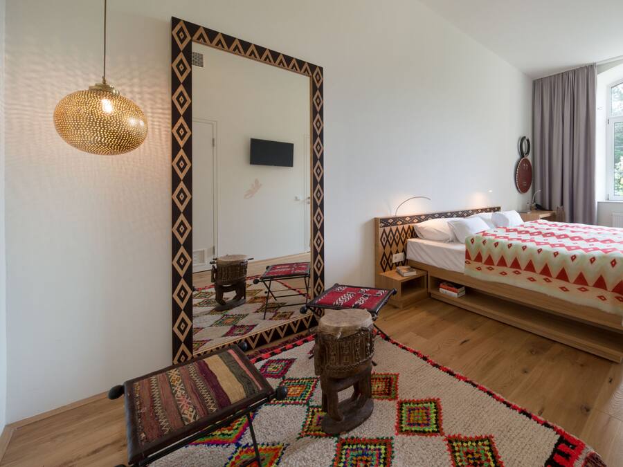 A bedroom with a bed, a large mirror, a television, a window with curtains, and a patterned rug.