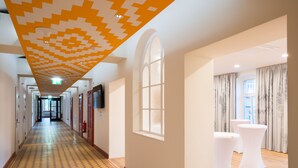 A hotel corridor with patterned flooring, a large arched window, and a seating area with white tables. - Gabrium (Maria Enzersdorf)