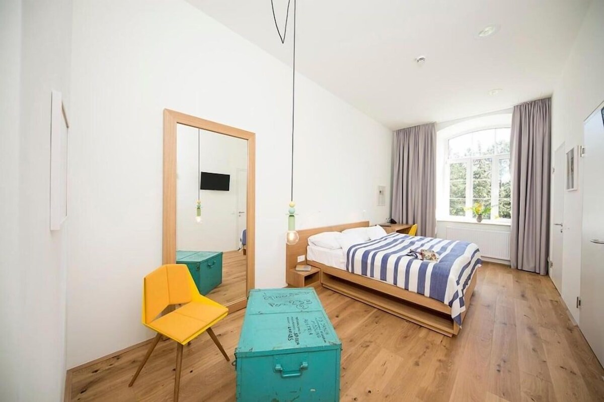 Un dormitorio con una cama, una silla, un espejo y una ventana.