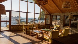 A room with large windows overlooking a beach, wooden furniture, and woven ceiling lamps.