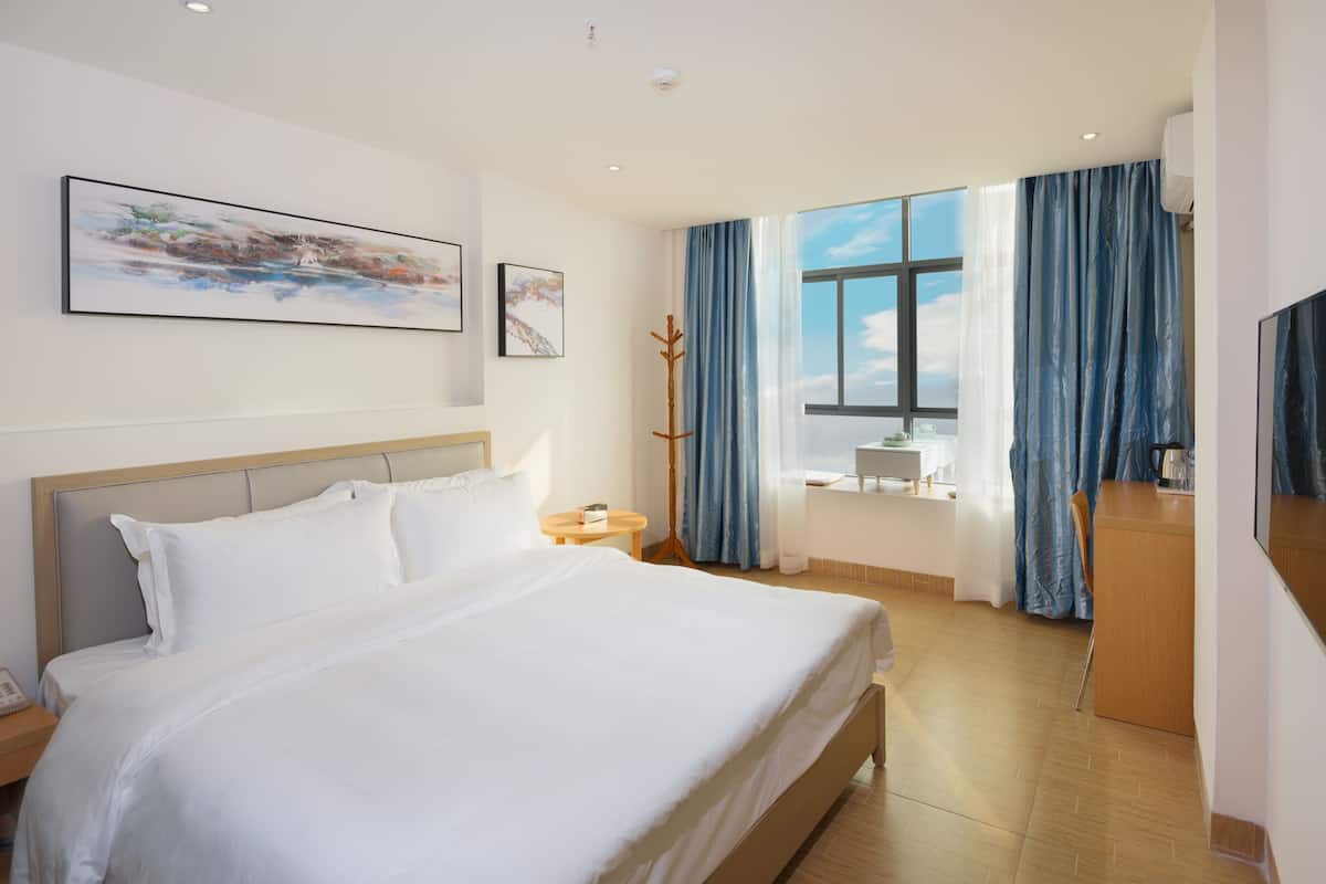 Une chambre d’hôtel moderne, dotée d’un grand lit, d’un bureau et d’une fenêtre avec des rideaux.