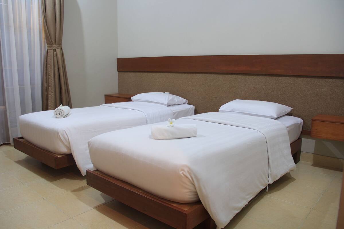 A hotel room with two single beds, each with a rolled towel and a flower.