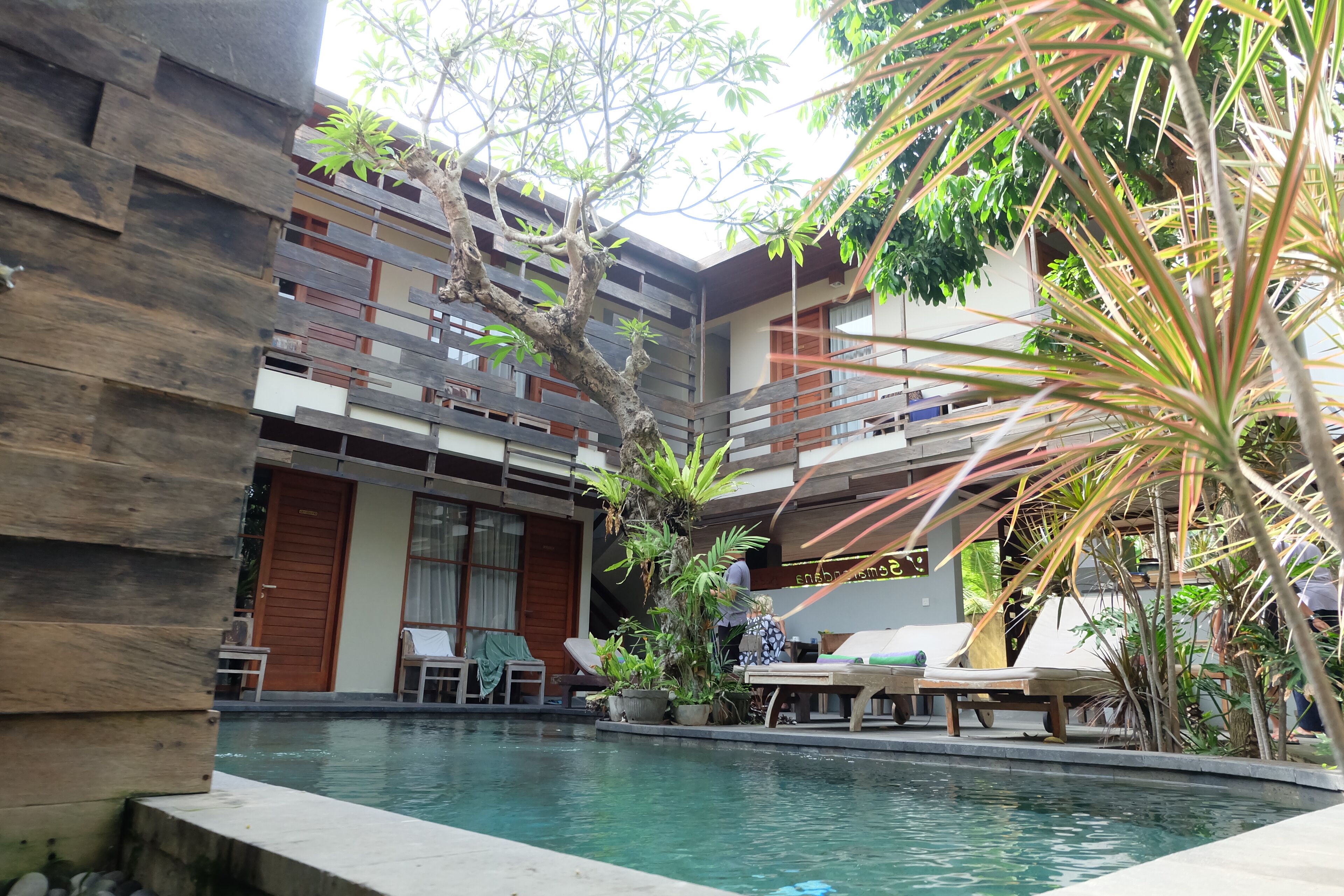A pool area with lounge chairs, a wooden deck, and a modern building with balconies.